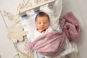 Newborn session portrait of a baby girl laying in a wooden blanket with a pink blanket.