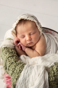 Newborn baby girl wearing a tiny bonnet and sleeping in a bucket.