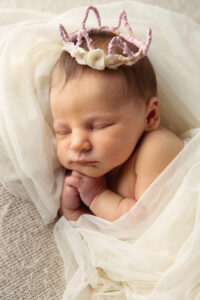 Close up portrait of a newborn wearing a tiny crown and wrapped in white silk.