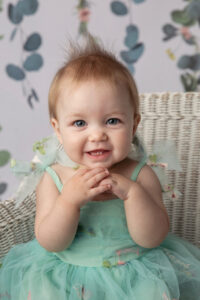 Cute closeup photo of a one year old sitting on a whicker chair and smiling.