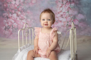 Milestone photo of a one year old girl sitting on a newborn prop and smiling.