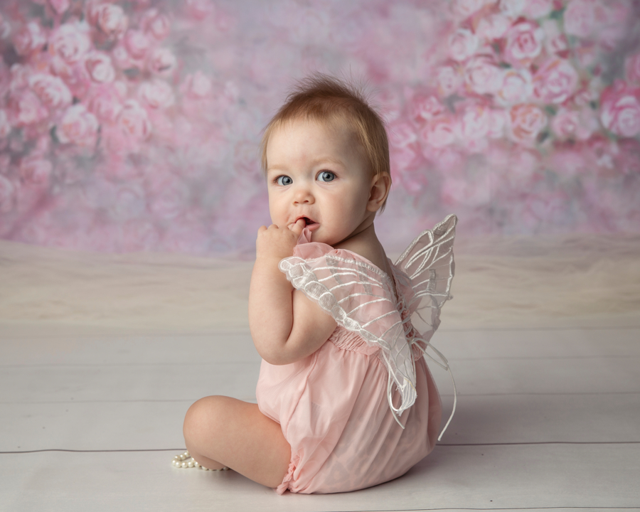 One year old with wings on her back looking over her shoulder for a portrait.