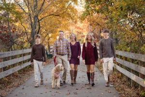 A family with teenage children walking on a path with their dog in the fall foliage. 