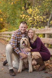 Couple with their dog photographed near a fence outdoors with fall foliage and ready to be printed at Raven's Wish.