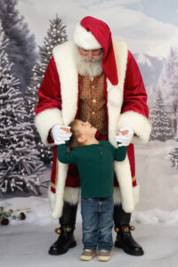 Portrait of a young boy with Santa Clause.  Boy is holding Santa's hands and looking up at him.