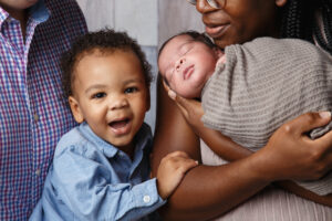 Close-up photo of newborn baby and big brother in parents arms.