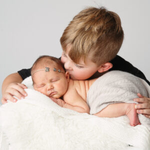 Portrait of a newborn with his big brother kissing his forehead while he sleeps.