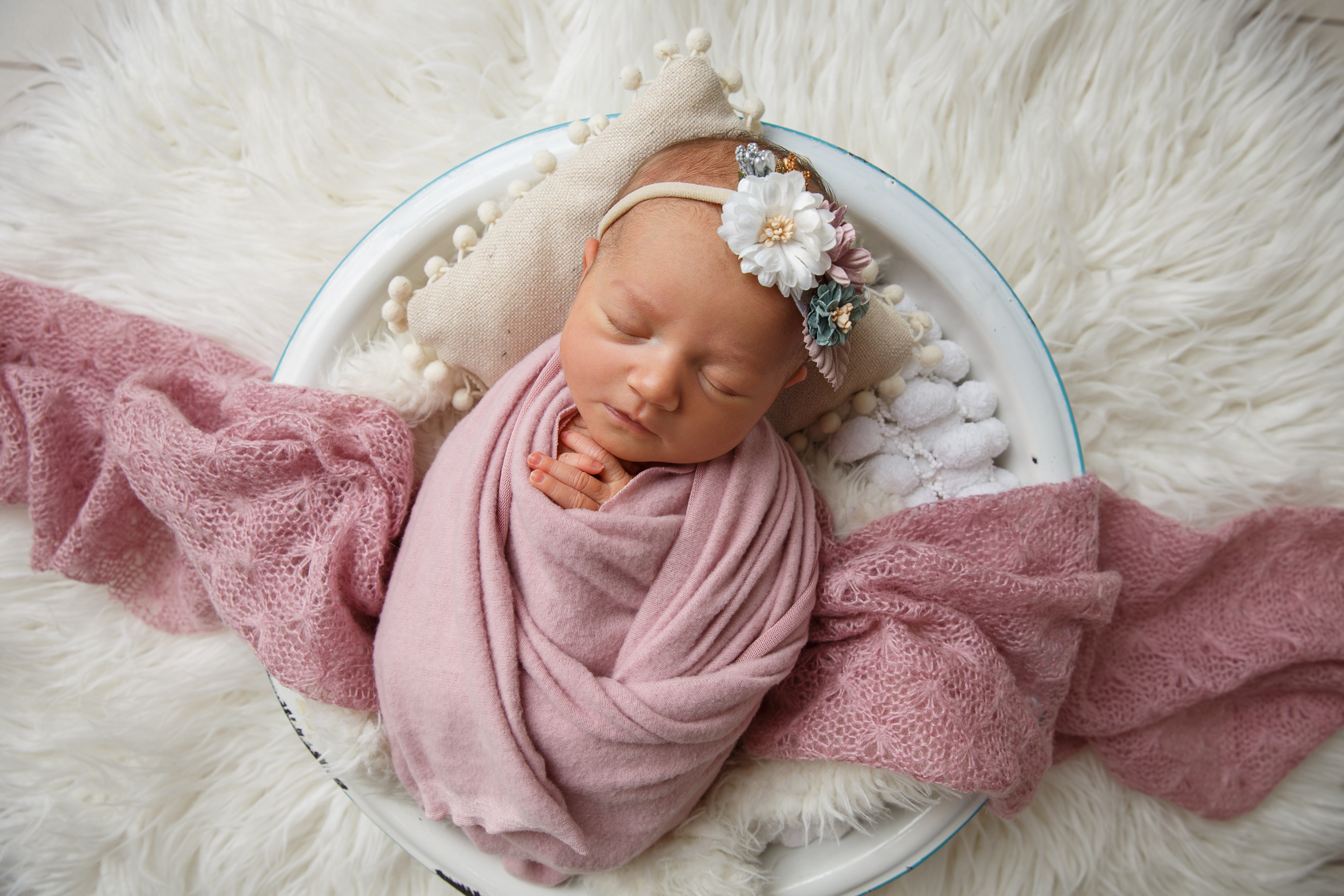 Posed portrait of a newborn baby wearing a pink wrap and laying in a white wicker basket.