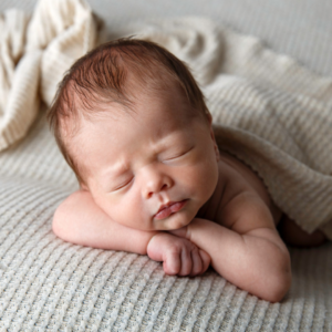 Professional baby portrait of a newborn laying on tummy with arms tucked under him and hands under his chin.