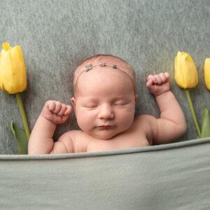 Newborn photo of a baby inside a blanket pocket with yellow tulips.