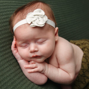 Newborn portrait of a baby girl laying on her side with her hands near her face on a green blanket 