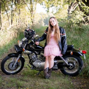 High School senior in a pink dress and a leather jacket standing with a motorcycle.