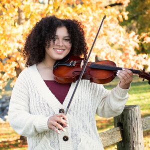 High school senior girl playing a violin in a fall landscape.