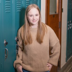 Image of a high school senior standing by a locker in the school hallway