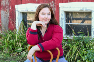 Close up image of a cute high school senior posed leaning on a chair outside of a red bard.