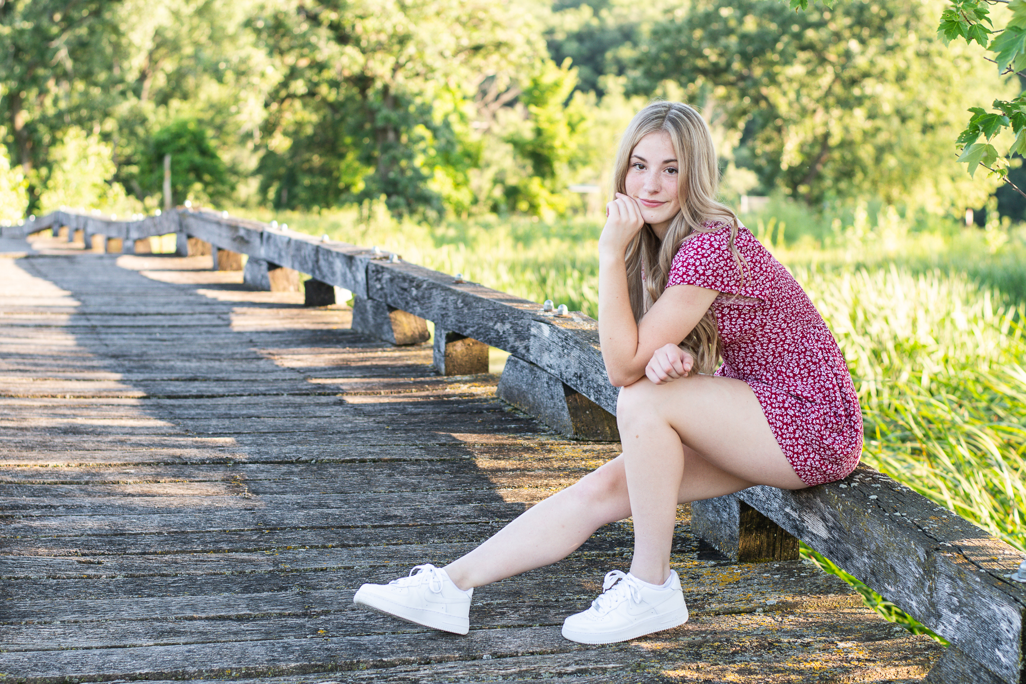 Pretty girl in a red jumper being photographed on a small bridge by professional senior photographer, life in Pink Photography