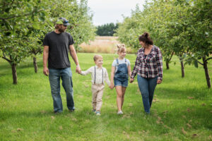 A portrait of a Family of four walking hand in hand in the apple orchard.