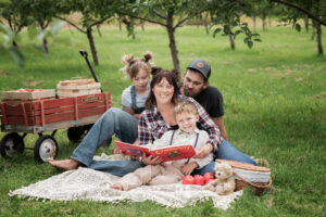 A family sitting on a blanket with a book and wagon.